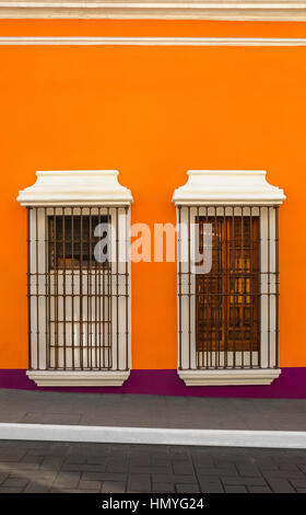 Two windows with bars on orange wall down the street Stock Photo