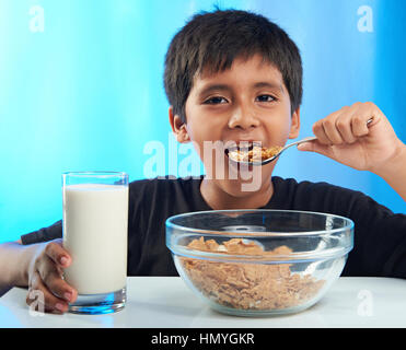 latino boy eating cereal isolated on blue background Stock Photo