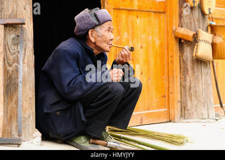 ZHAOXING, CHINA - NOVEMBER 11:  Old Chinese resting on the doorstep of his cottage smoking a pipe in the village Zhaoxing on November 11, 2010 Stock Photo