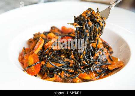 Black spaghetti sauce on fork, chili, seafood with raw tomato in white disk. Stock Photo