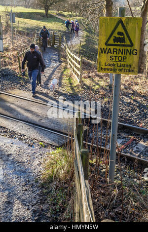 'Warning. Stop, look, listen, beware of train' sign. Walkers using a pedestrian crossing on a single track railway line, Hope, Derbyshire, England, UK Stock Photo