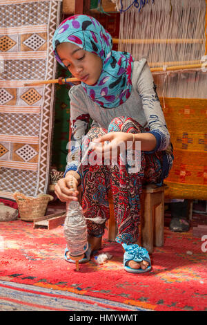 Morocco.  Young Amazigh Berber Girl Working with Wool on a Spindle.  Ait Benhaddou Ksar, a World Heritage Site. Stock Photo