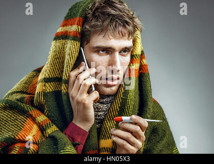 Sick man wrapped in blanket with a high temperature calling on the phone. Man suffering cold and winter flu virus. Health care concept Stock Photo