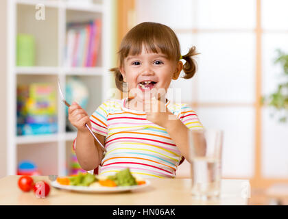 Funny child girl has a dinner in kindergarten or nursery room Stock Photo