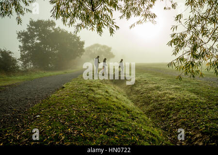 Three people walking in the fog. Taken in the autumn on a foggy but bright morning in October. Stock Photo