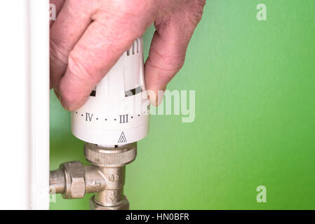 Man regulating a radiator thermost valve.Turning down heating to save energy. Stock Photo