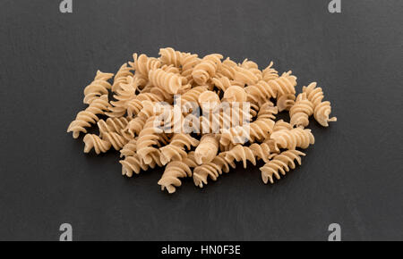 A portion of uncooked brown rice pasta fusilli atop a slate background. Stock Photo