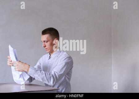 Entrepreneur adds documentation and completes work day. Men with short hair and blond hair sitting on chair at white table in office and dressed in wh Stock Photo