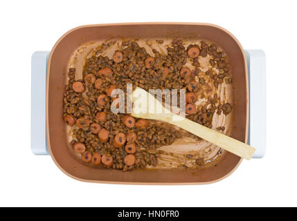 Top view of baked beans and sliced hot dogs in a ceramic skillet with a wood spoon isolated on a white background. Stock Photo