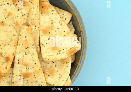 Top close view of pizza crust chips in an old stoneware bowl atop a blue fabric tablecloth. Stock Photo