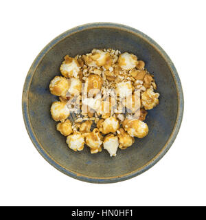 An old stoneware bowl with toffee caramel popcorn crumbs with nuts isolated on a white background. Stock Photo