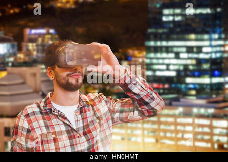 Casual man man holding virtual glasses against glowing modern buildings in city Stock Photo