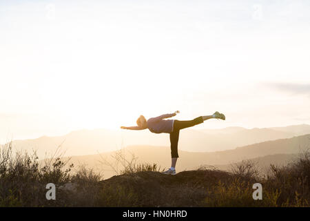 A woman practices yoga high on a ridgeline of the Santa Monica Mountains, silhouetted by the setting sun. Stock Photo