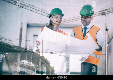 Crane and building construction site against smiling architects looking at blueprint in office corridor Stock Photo