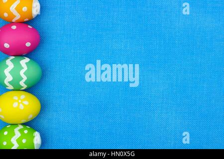 Colorful Easter egg side border over a blue burlap background Stock Photo
