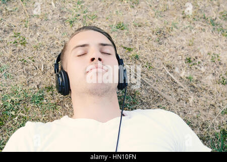 Young attractive man listening to music with headphones in a park. Outdoors. Stock Photo