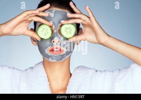 Young woman with a clay mask. Photo of attractive young woman covering her eyes with cucumbers on a blue background. Grooming himself Stock Photo