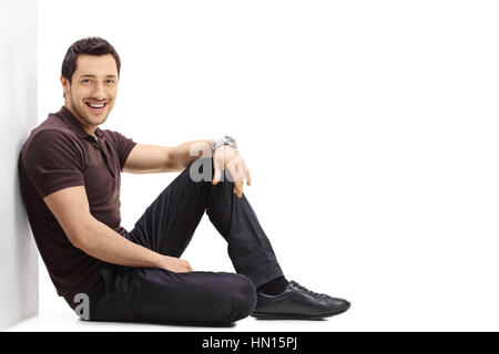 Young guy sitting on the floor and leaning against a wall isolated on white background Stock Photo