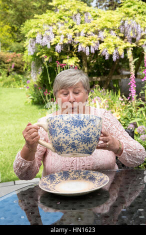 Woman drinking tea from a very large china cup in a Devonshire garden Stock Photo