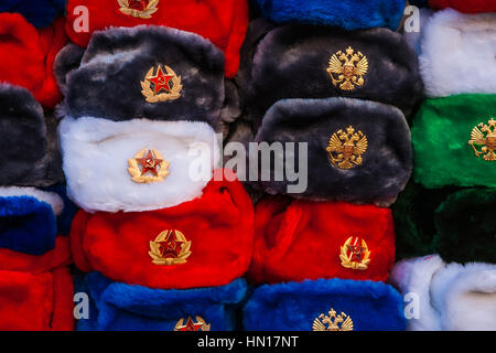 Pile of traditional Russian winter fur caps with ear-flaps displayed for sale as souvenirs. Red, white, blue, black, green caps Stock Photo