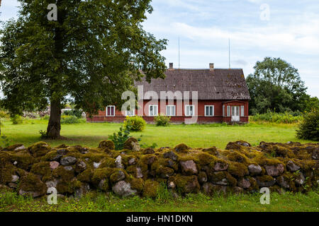 Old red wooden house with stoned fence in Estonian village Stock Photo