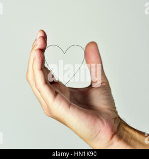 closeup of the hand of a young caucasian man holding the profile of a heart, against an off-white background Stock Photo
