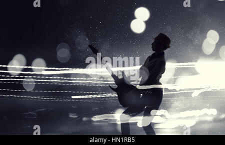 Silhouette of woman with guitar against bokeh lights background Stock Photo