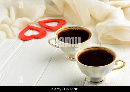 Two cups of morning fragrant coffee on St. Valentine's Day against the background of two red hearts and a white scarf Stock Photo