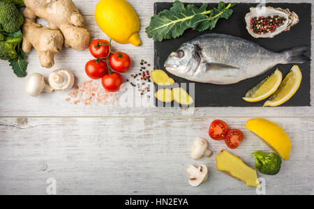 Useful dorado fish, rich in protein, vitamins, Omega 3 with vegetables, lemon and ginger, prepared for cooking on a white wooden table. Top view Stock Photo