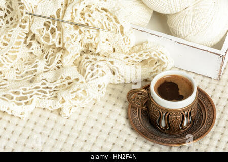 crochet tablecloth, crochet hooks, balls of cotton thread and cup of black coffee on a white woolen plaid Stock Photo