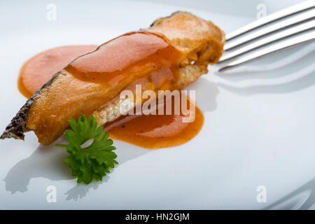 Marinated herring fish in tomato sauce on plate with parsley and fork in background Stock Photo