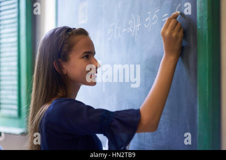 Young people and education. Group of hispanic students in class at school during lesson. Portrait of happy girl doing math exercise at blackboard Stock Photo