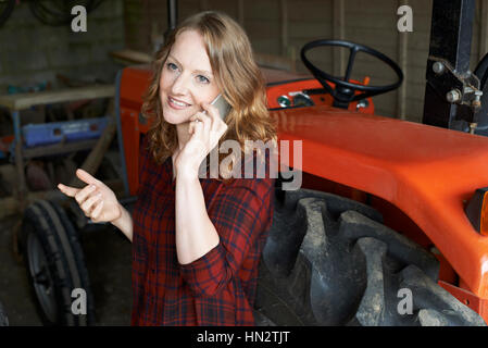 Female Agricultural Worker With Tractor Making Phone Call Stock Photo