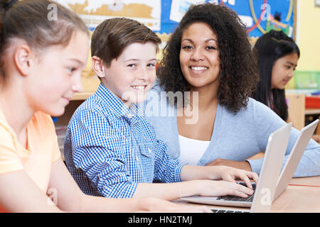 Teacher Helping Group Of Elementary School Children In Computer Class Stock Photo