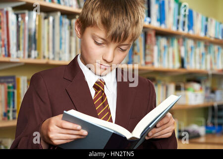 Boy Wearing School Uniform Reading Book In Library Stock Photo