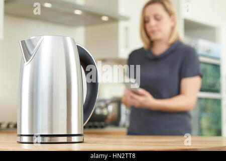Woman Controlling Smart Kettle Using App On Mobile Phone Stock Photo