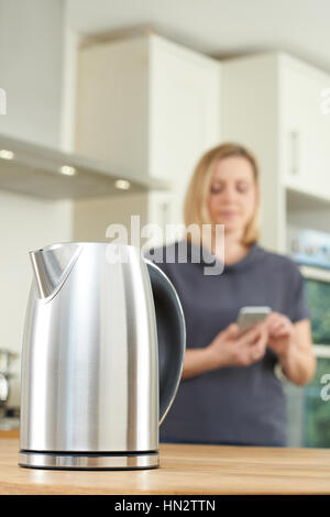 Woman Controlling Smart Kettle Using App On Mobile Phone Stock Photo