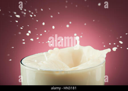 close up of milk splash in glass isolated on pink background Stock Photo