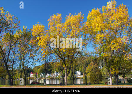 Trees showing yellow fall colors and white houses in town along lake in New England's Adirondack Mountains, upstate New York, USA Stock Photo