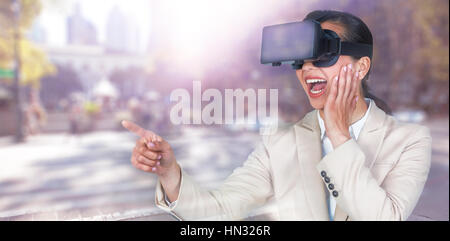 Excited businesswoman pointing while wearing virtual video glasses against blurred new york street Stock Photo