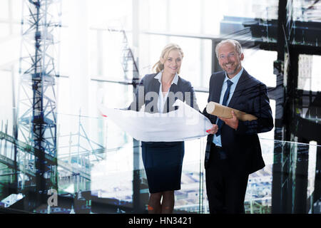 Work in progress in the city against portrait of business colleagues standing with blueprint in corridor Stock Photo