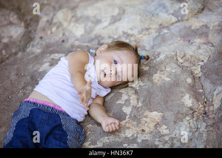Little girl lying on rock and stretching out hand. Playful mood or asking for help concept. Stock Photo