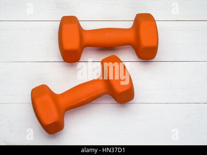 Two orange plastic coated dumbbells on white wooden background Stock Photo