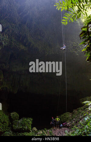 A Young Woman Rappels Into A Deep Dark Cave In A Forest In Puerto Rico Stock Photo