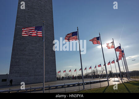 Setting sun illuminates American flags, especially flag against shadowed Washington Monument.  Airplane in sky on right Stock Photo