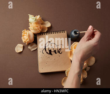 Valentine's Day concept. Diary or notebook with word love written by female. Female's hand writing in diary with brown pages over brown background. Stock Photo