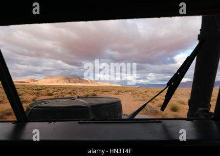 View from the drivers position of an four by four oldtimer off-road vehicle driving off- road in a stone desert in Morocco. You can see the spare whee Stock Photo