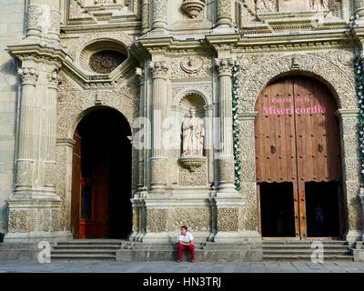 Young man sitting on ledge in front of the Cathedral of Our Lady of the Assumption, Oaxaca City, Oaxaca, Mexico Stock Photo