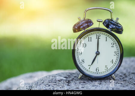 clock in the green nature background, retro bell clock time at 7 o'clock. Stock Photo