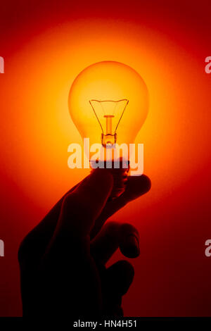 light bulb, silhouette hand hold Clear Glass Tungsten lighting bulb or Twisted Candle bulb on red color background. Stock Photo
